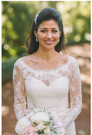 A bride wearing a lace dress holding flowers wearing a pearl earrings