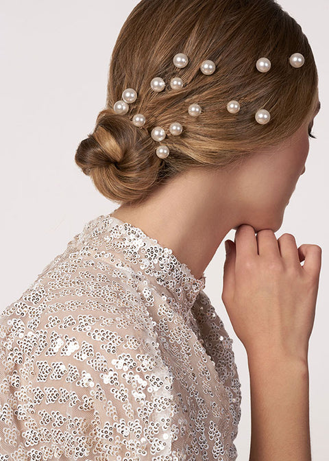 model with low bun wearing scattered pearl bridal hairpins across her hair (side view)