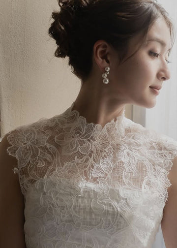 Close-up of a person wearing a white lace garment and pearl earring with a neutral background