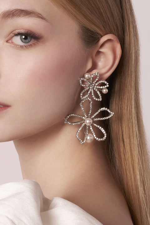 Close-up of a woman wearing a floral earring with pearls on a light background