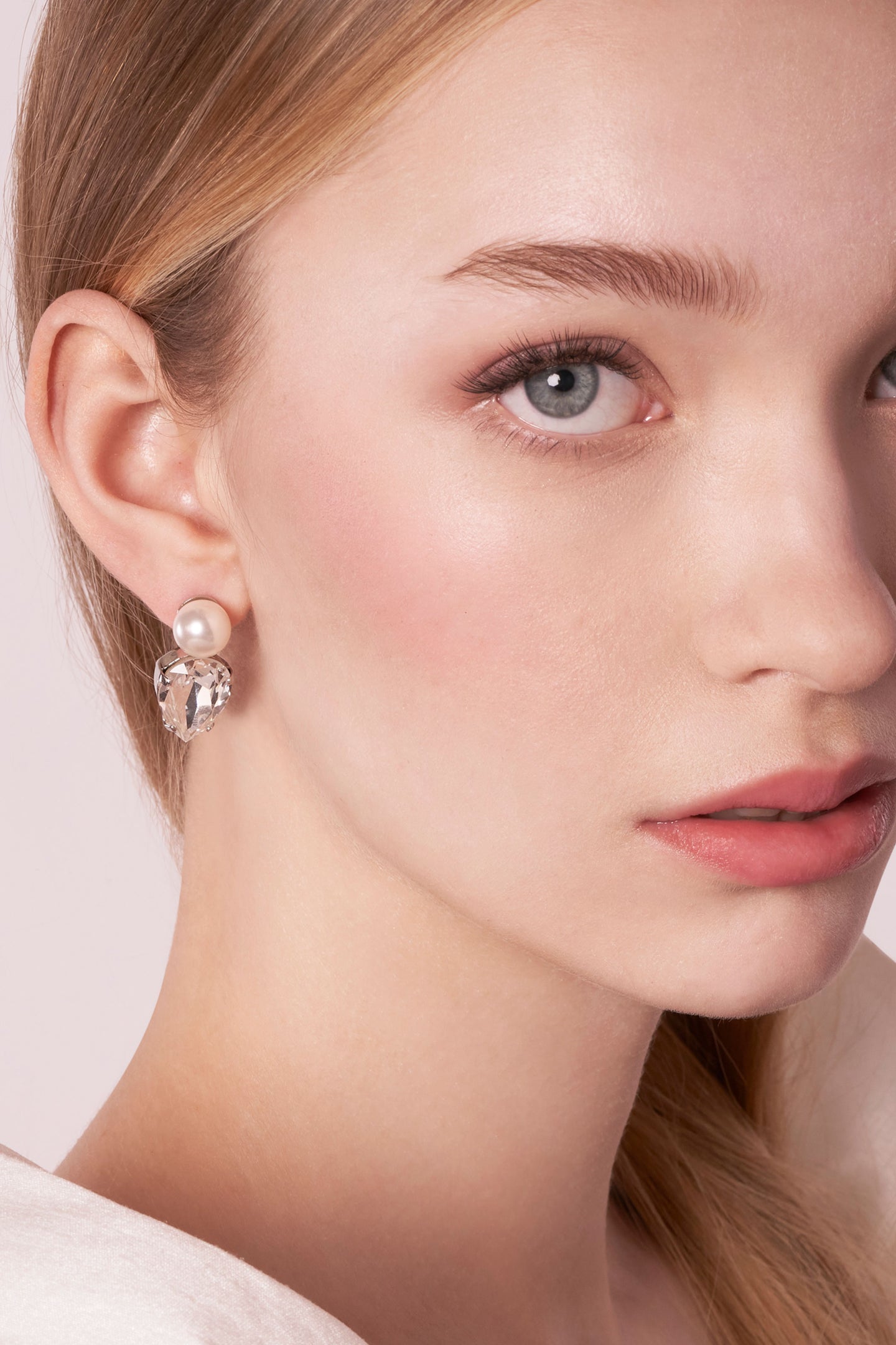 Close-up of a woman wearing a pearl earring with a plain background
