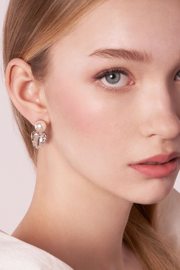 Close-up of a woman wearing a pearl earring with a plain background