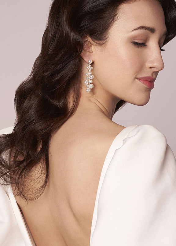 Woman wearing a white blouse with a deep neckline, showcasing a pearl earring.