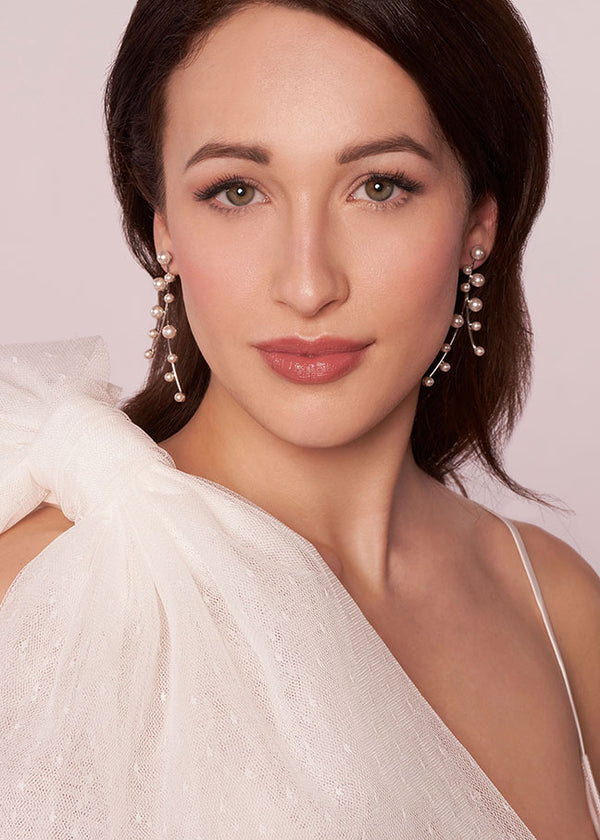 Woman wearing pearl earrings with a white top against a light pink background