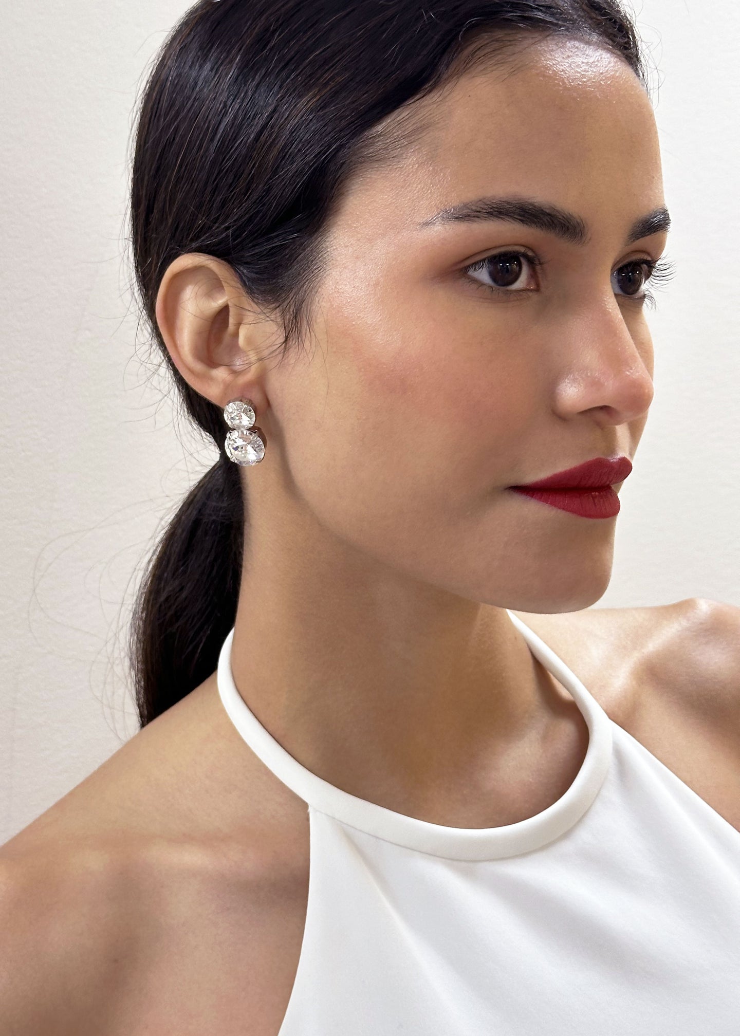 a lady in red lipstick wearing a sleek hair style and a pair of crystal stud earrings