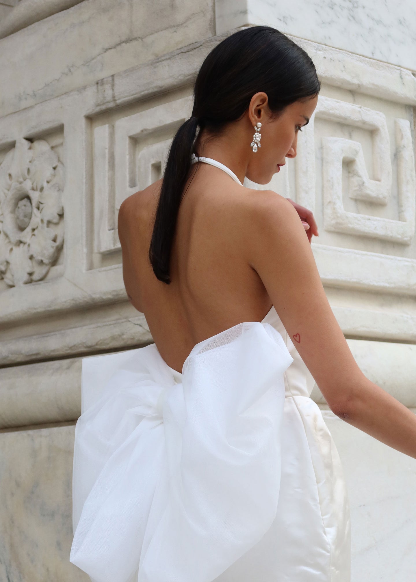 a lady in a bow wedding dress and crystal drop earrings outside the new york public library