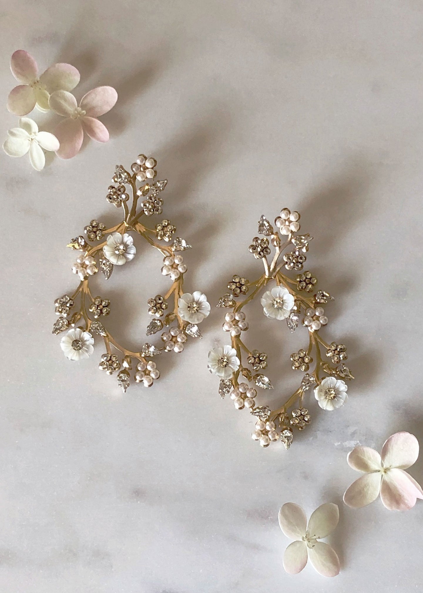 Mother of pearl floral earring on marble with scattered flowers surrounding