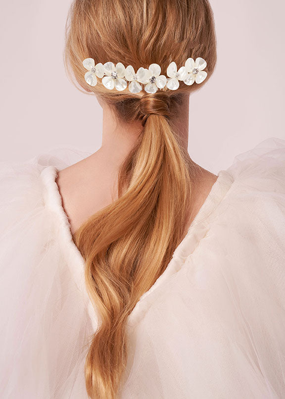 Woman with blonde hair styled in a ponytail with a decorative hairpiece against a light background