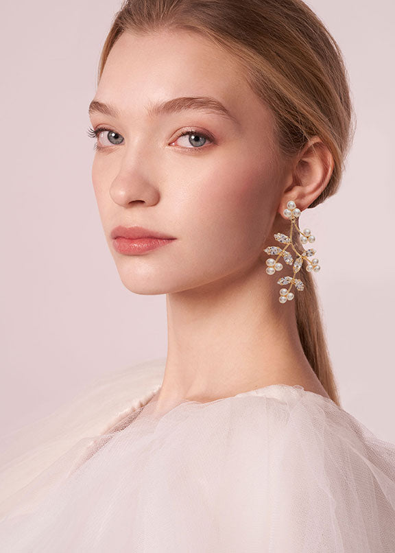 Close-up of a woman wearing elegant earrings against a soft pink background