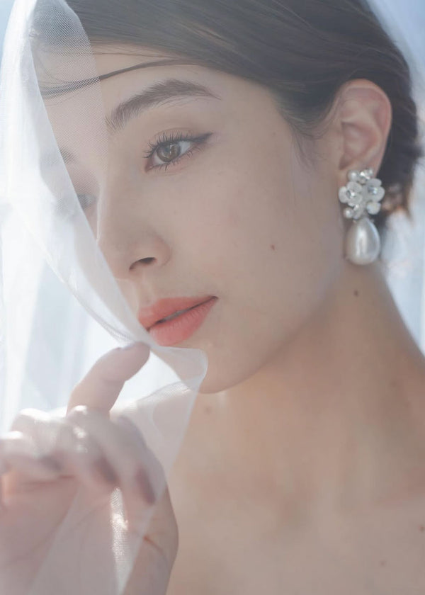 A close up view of a lady in a veil wearing floral pearl teardrop earrings.