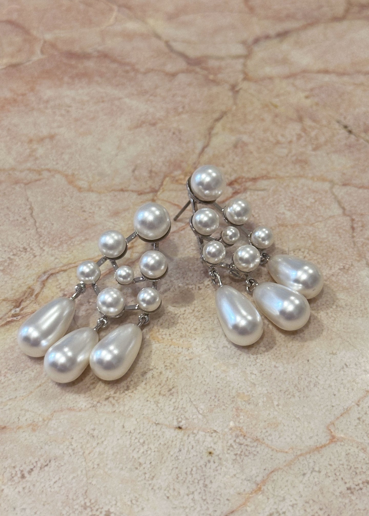 Pearl chandelier earrings laid out on a piece of blush marble