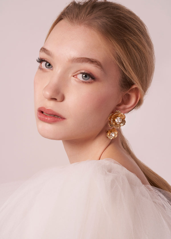 Model wearing double flower gold earrings on a neutral background