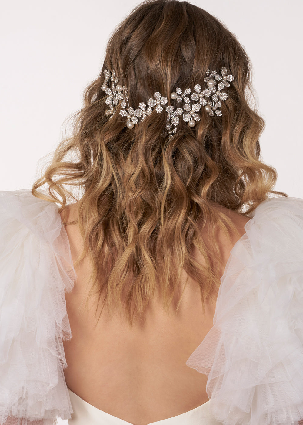 model with lose curls wearing statement floral hairpiece and tulle wedding dress (back view)