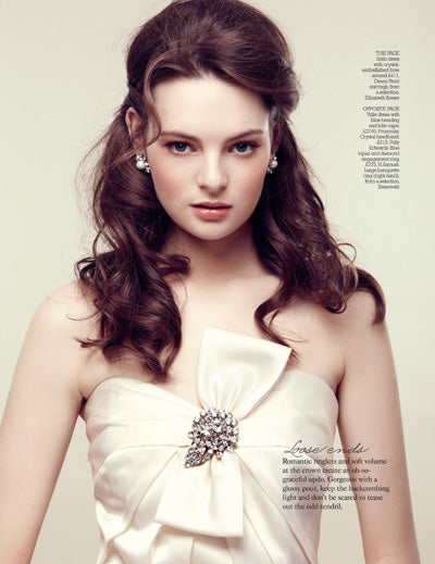 a model wearing a taffeta dress and a pair fo crystal and pearl earrings against a beige background 