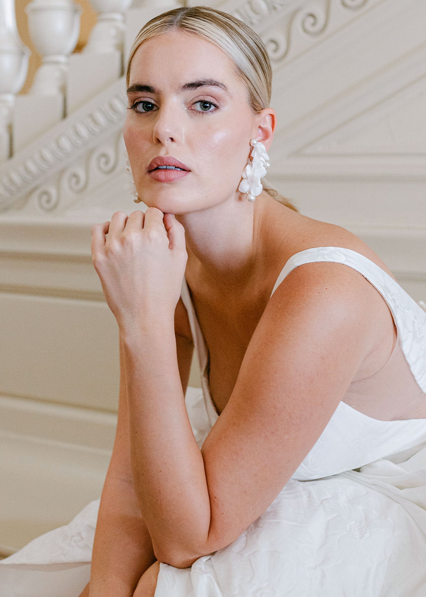 A lady with a slek haristyle wearing a pair of silk floral and pearl earrings. 