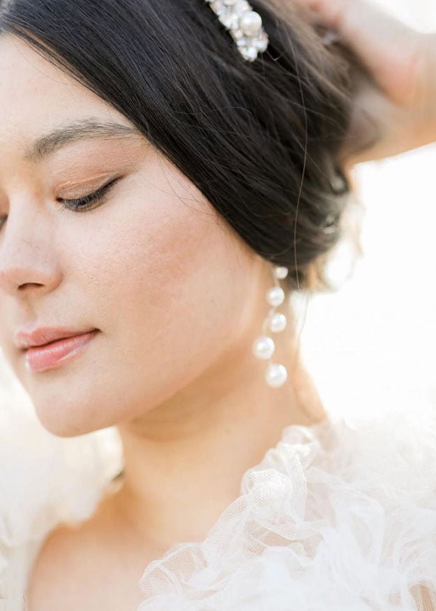 A modern linear silver pearl earring with 5 graduating pearls on a model in a tulle wedding dress (close up left view)