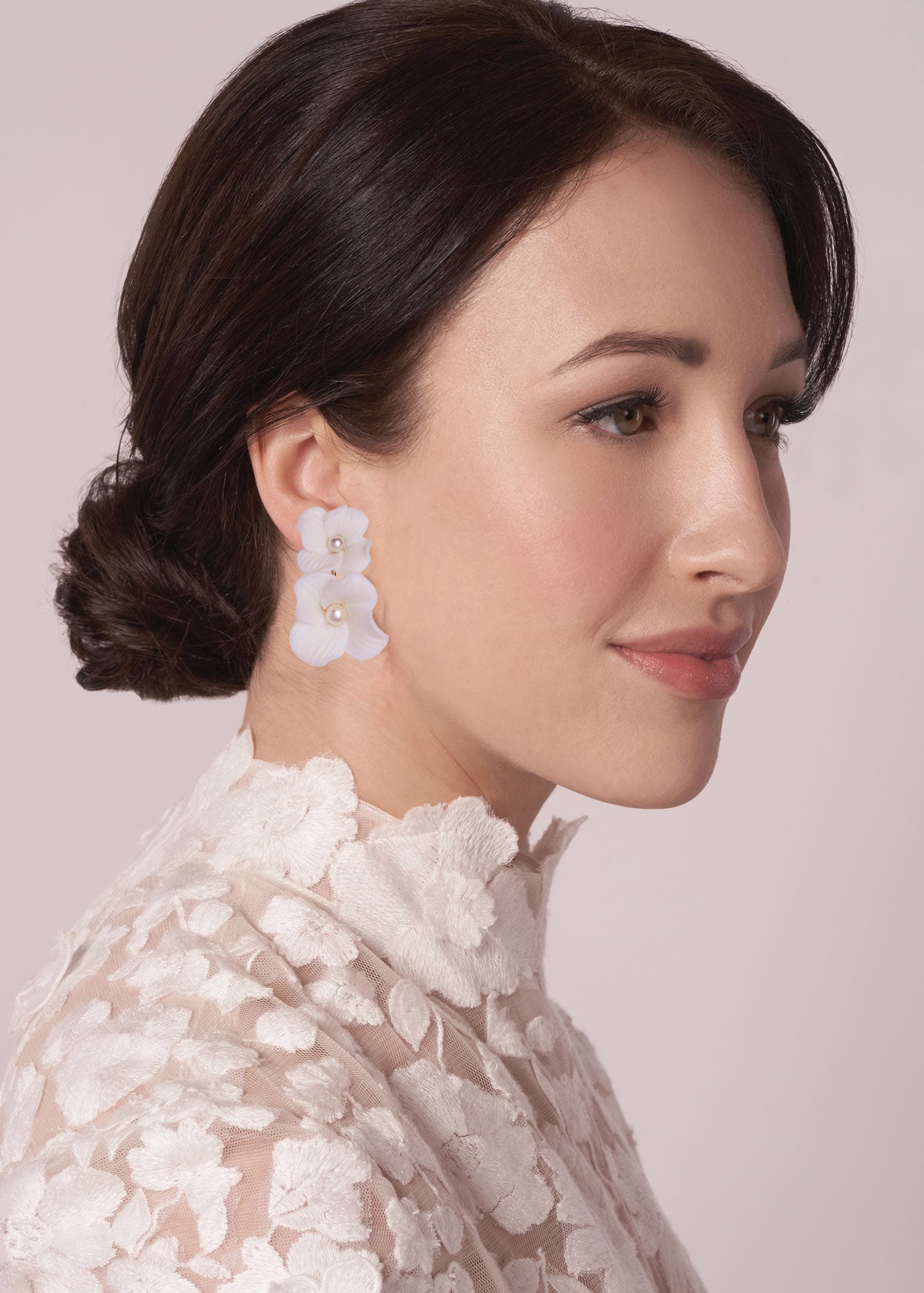 Woman wearing floral earrings with a white lace top against a light background
