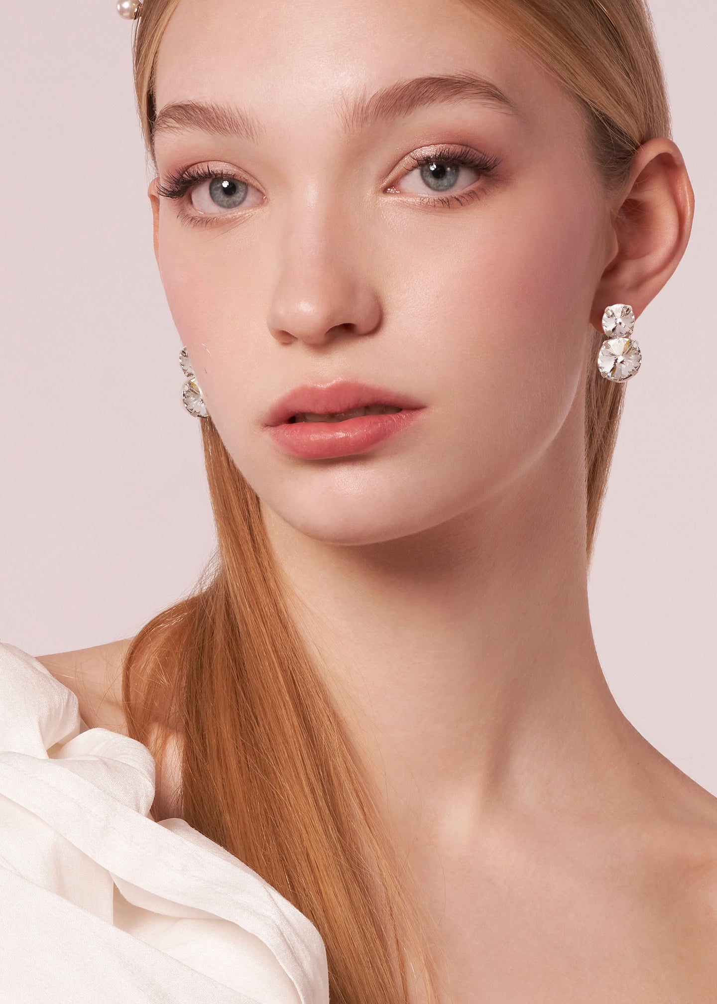 a lady wearing a modern double crystal stud earring against a beige background