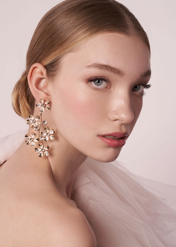 Woman wearing floral earrings with a soft pink background