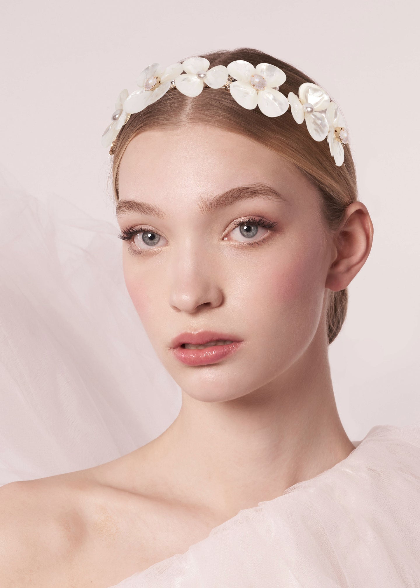 a close up of a lady wearing a mother of pearl floral headband set against a blush background