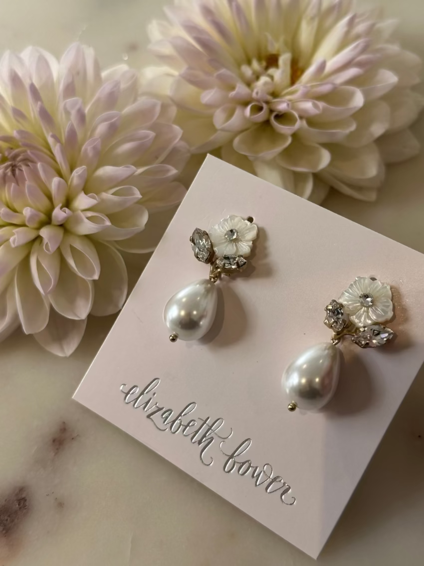 Pair of pearl earrings on a display card with flowers in the background