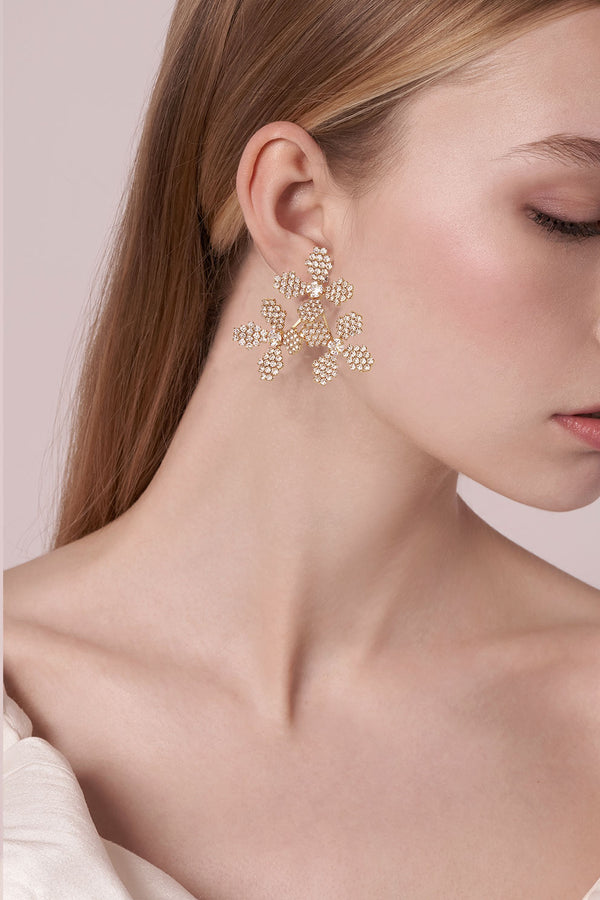Close-up of a woman wearing gold floral earrings against a neutral background