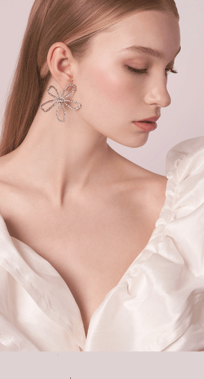 side view of a lady wearing floral crystal earrings on a blush background