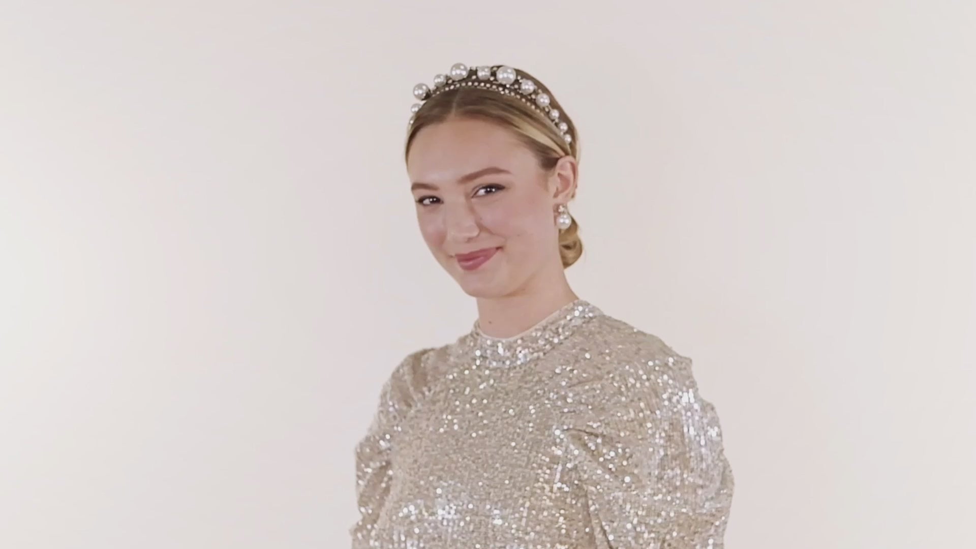 A lady smiling and dancing wearing a silver sequin dress and pearl headband