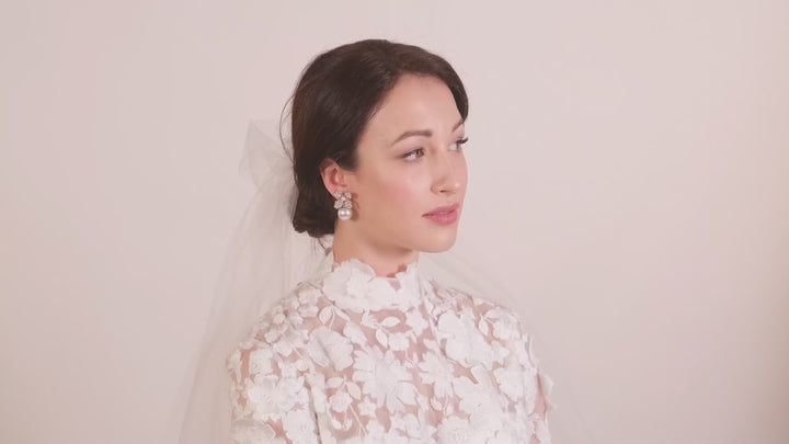 A lady wearing a lace wedding dress and veil and a pair of crystal floral and pearl bridal earrings