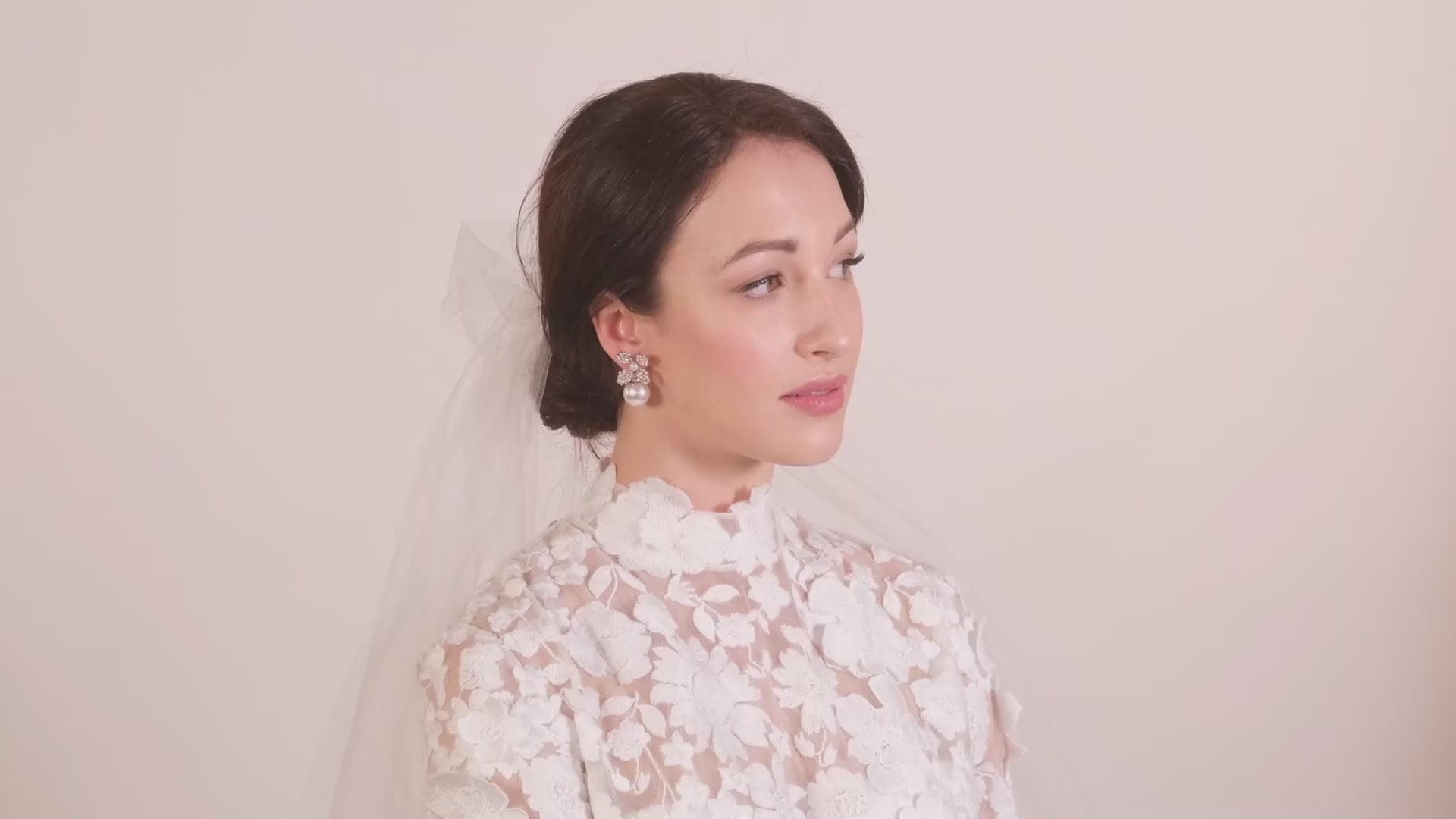 A lady wearing a lace wedding dress and veil and a pair of crystal floral and pearl bridal earrings