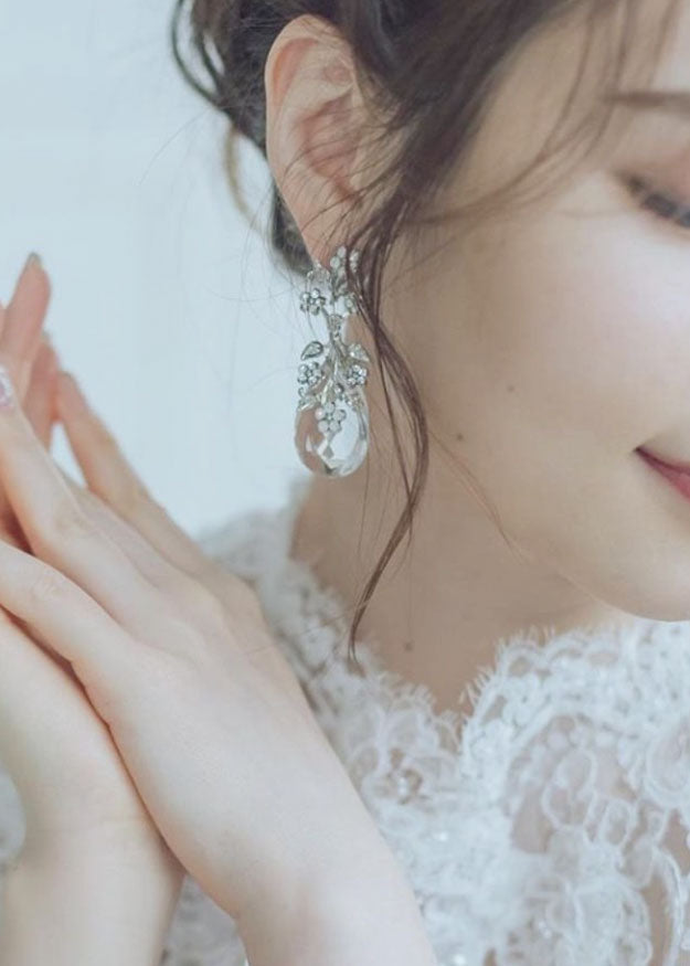 a close up of a woman wearing crystal teardrop earrings in lace dress. 