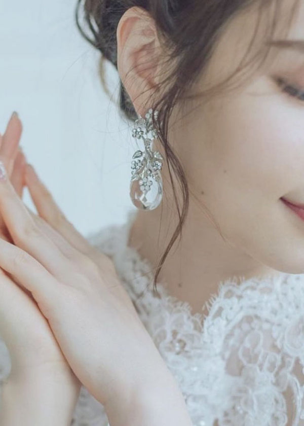 a close up of a woman wearing crystal teardrop earrings in lace dress. 