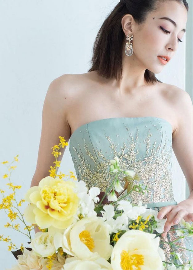 a japanese model wearing crystal teardrop earrings whilst holding yellow flowers. 