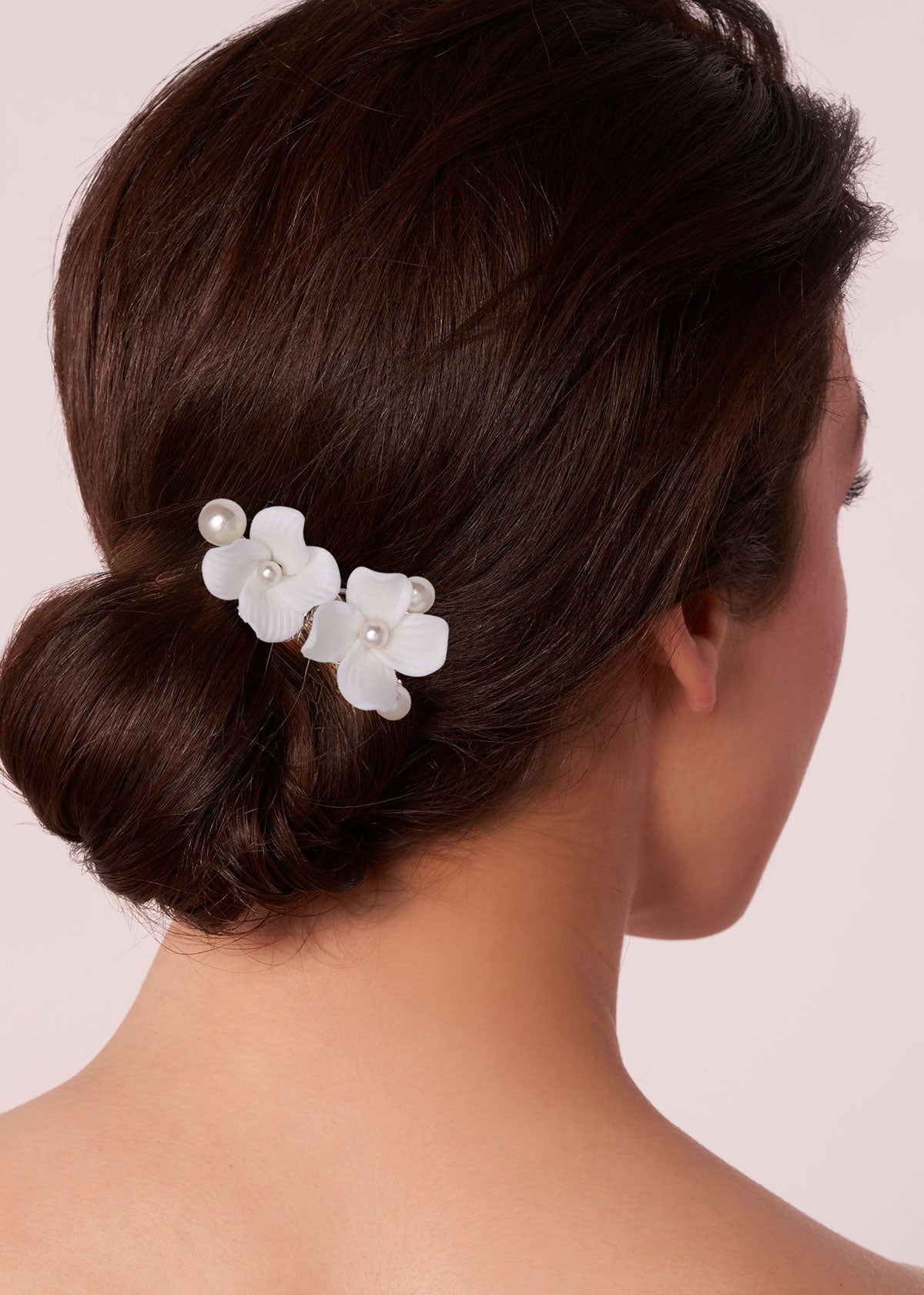 Woman with a styled hair bun wearing white floral hair clips on a light pink background