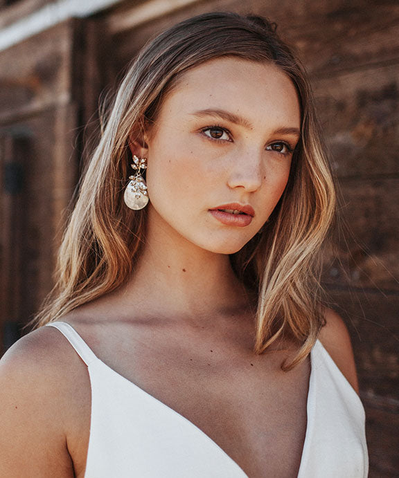 Woman with windswept hair wearing pearl and crystal drop earrings. 