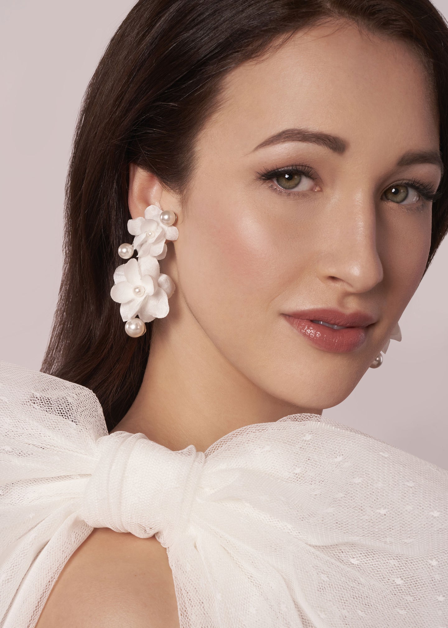 A pair of floral pearl earrings on a model wearing a bow accented wedding dress