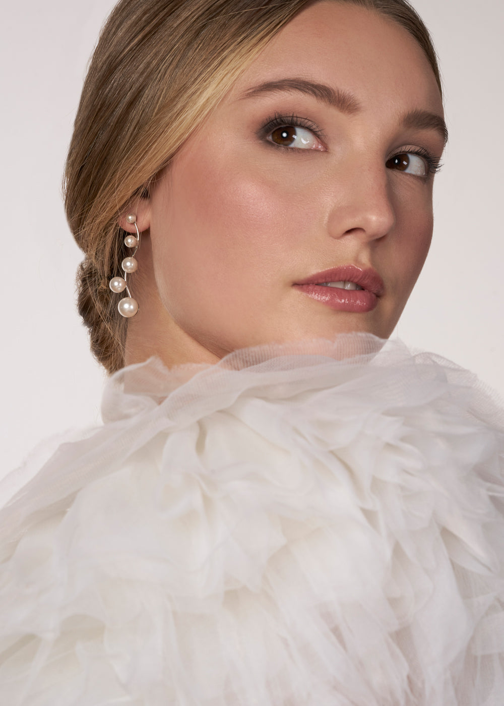 A modern linear silver pearl earring with 5 graduating pearls on a model in a tulle wedding dress (close up side view)